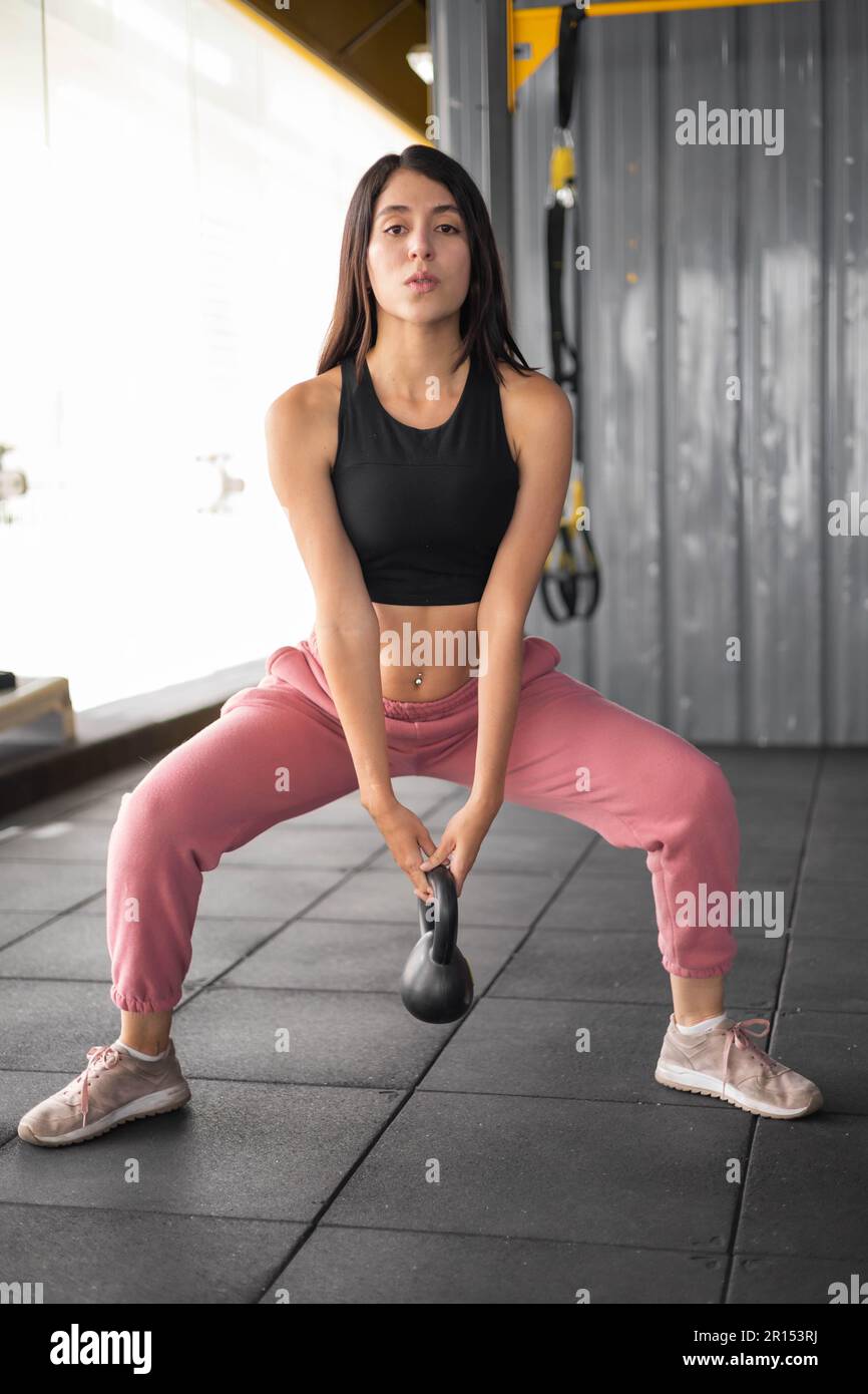 healthy physical activity, young latin woman with long hair wears sports top and leg warmer, gym with weights equipment, routine exercise Stock Photo