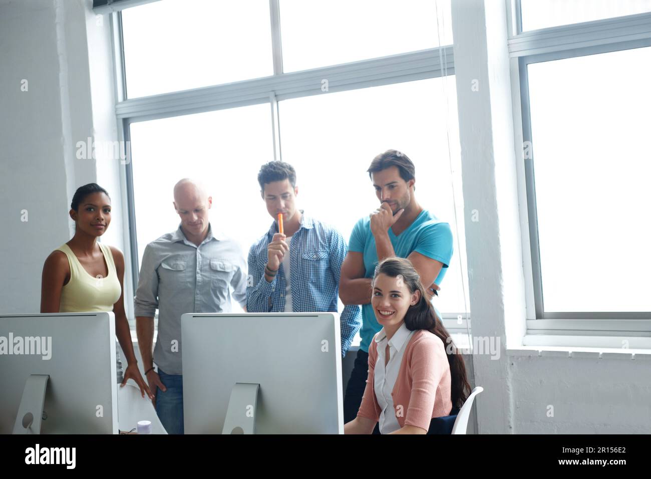Problem solving is their pleasure. A group of designers standing in a office together around a computer screen to run over their plans. Stock Photo