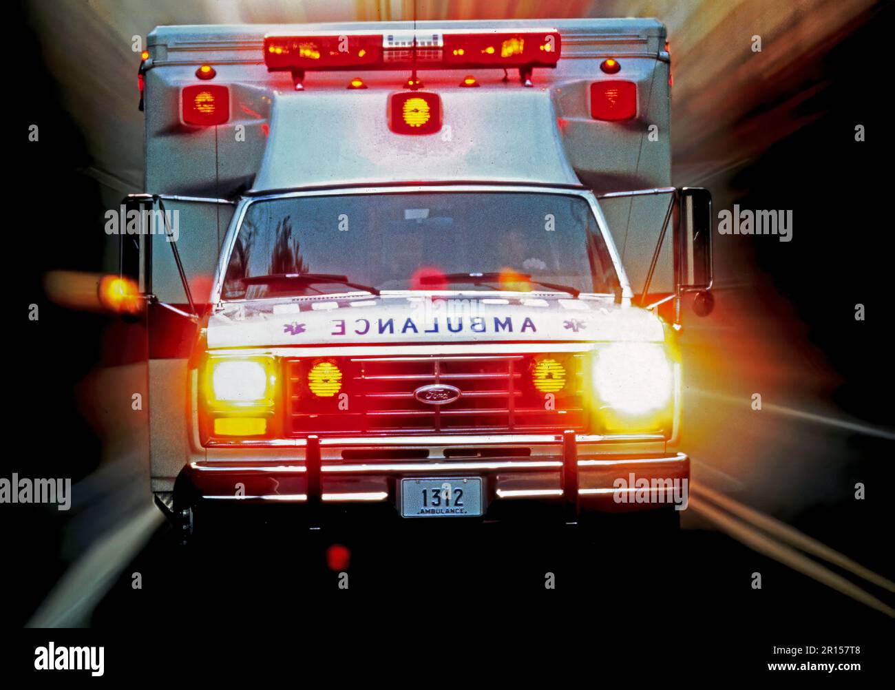 Motion blur image of a speeding ambulance with  flashing lights rushing directly towards the camera on a two-lane highway Stock Photo