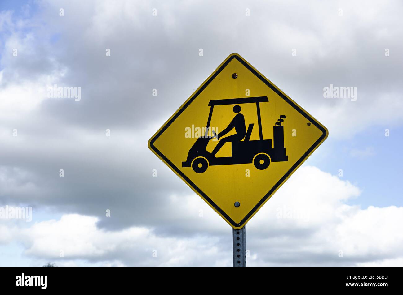 yellow and black golf cart crossing road sign with cloudy sky Stock Photo