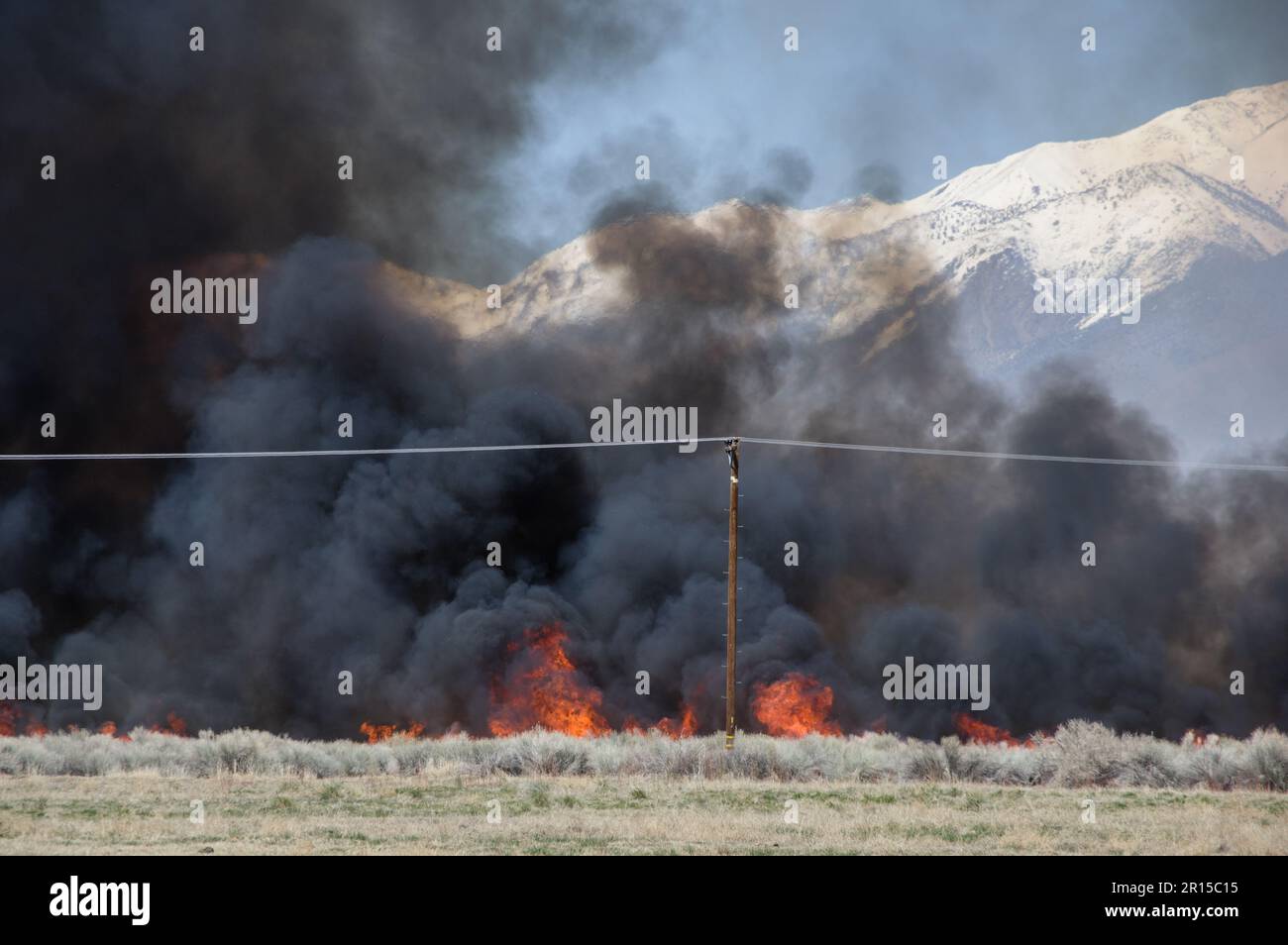 wildfire and smoke burning in sagebrush behind power poles Stock Photo