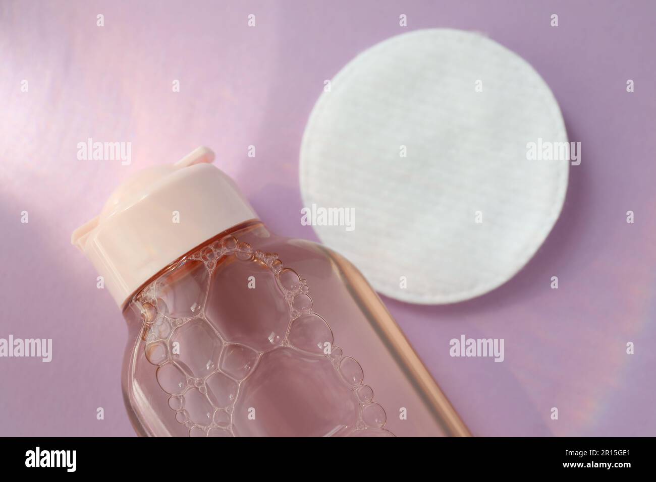 Bottle of micellar water and cotton pad on pink background, closeup Stock Photo
