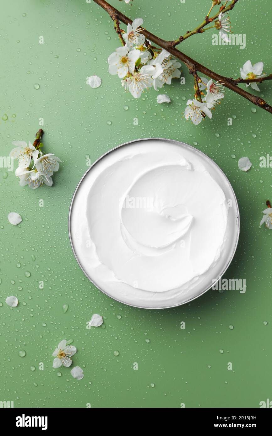 Flat lay composition with jar of face cream and flowers on wet green ...