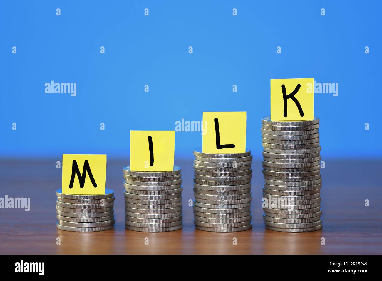 A row of a growing stack of coins illustrating the increasing cost of Milk due to the rising cost of living, on a blue background with copy space Stock Photo