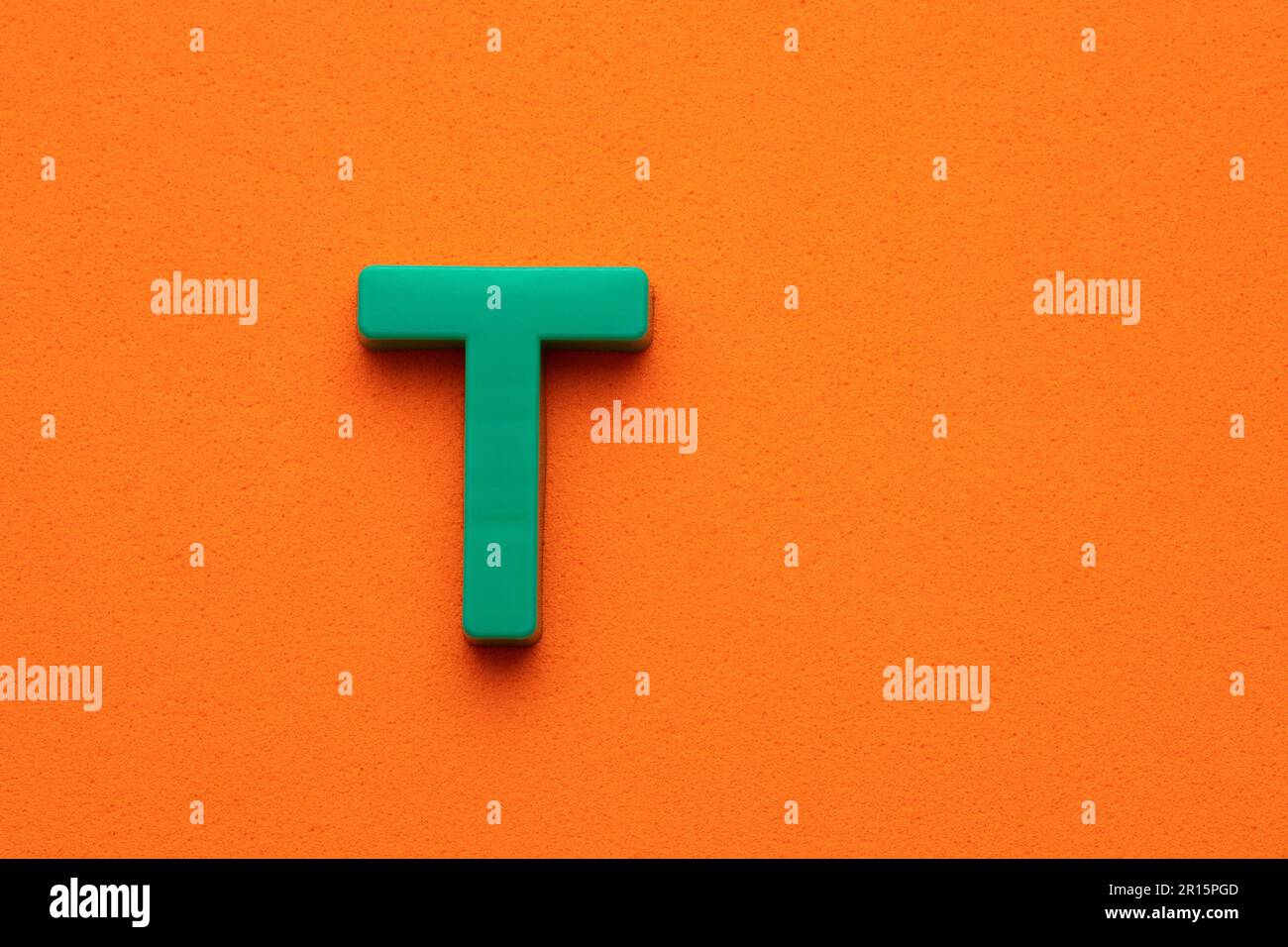 Alphabet letter T - Green plastic piece on orange foamy background ...