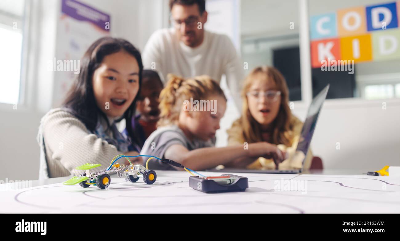school girl learns about programming and computer engineering as she watches a robotic car operate on a code. Class of primary school students develop Stock Photo