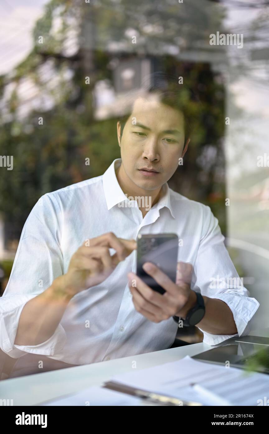 Portrait of a focused and professional millennial Asian businessman or male CEO checking his messages on his smartphone while working in his office. Stock Photo