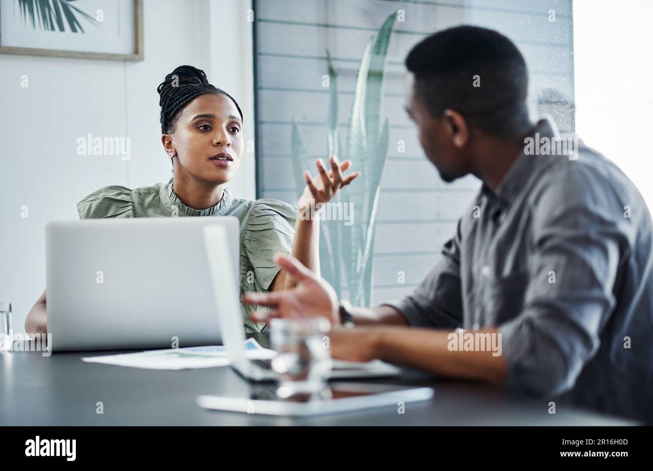 How can we overcome this problem. two young businesspeople sitting together in the office and having a discussion while using technology. Stock Photo