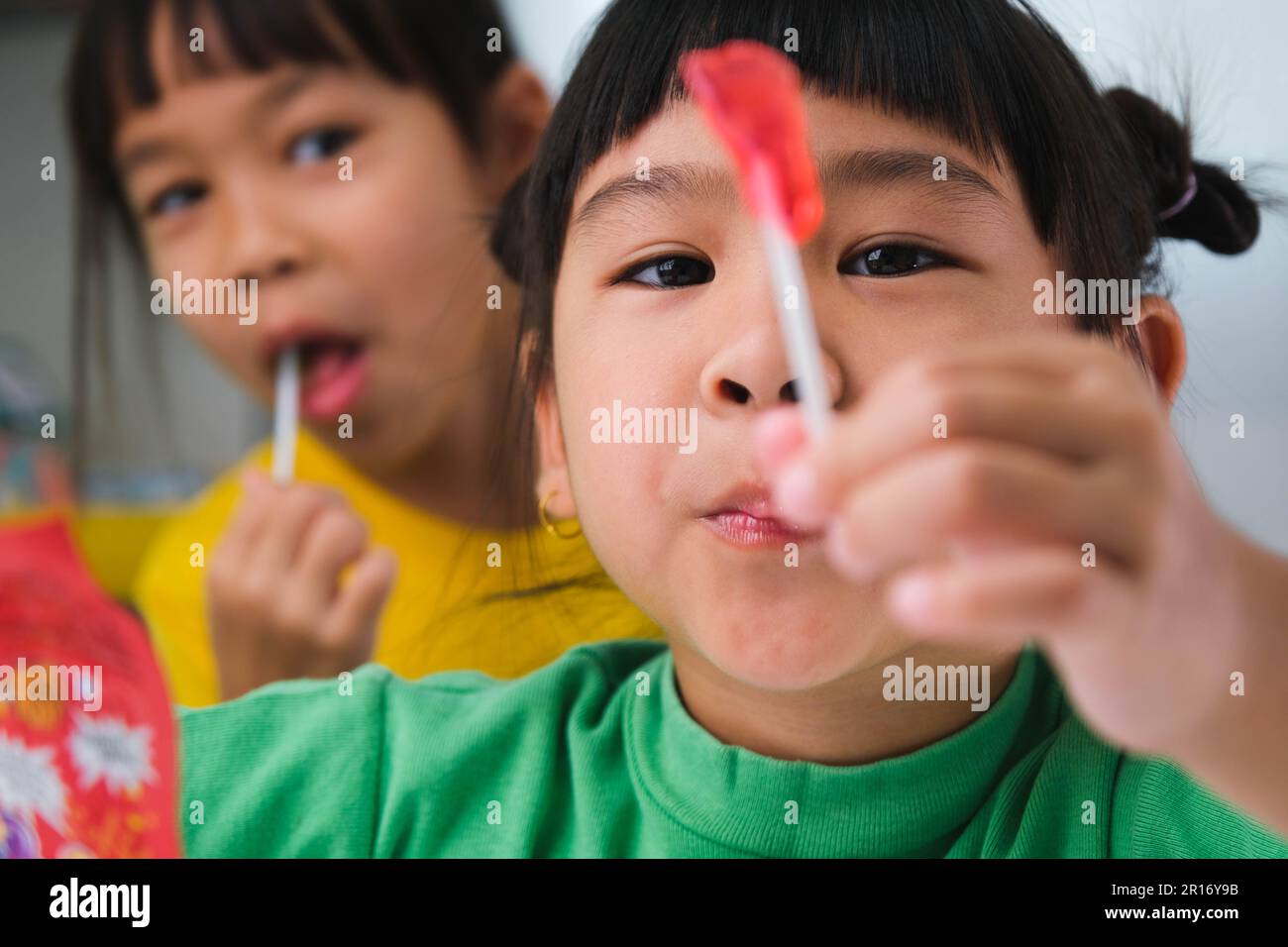 Two happy cute little girls eating lollipops. Funny kid with lollipop candy. Child eating sweets. Stock Photo