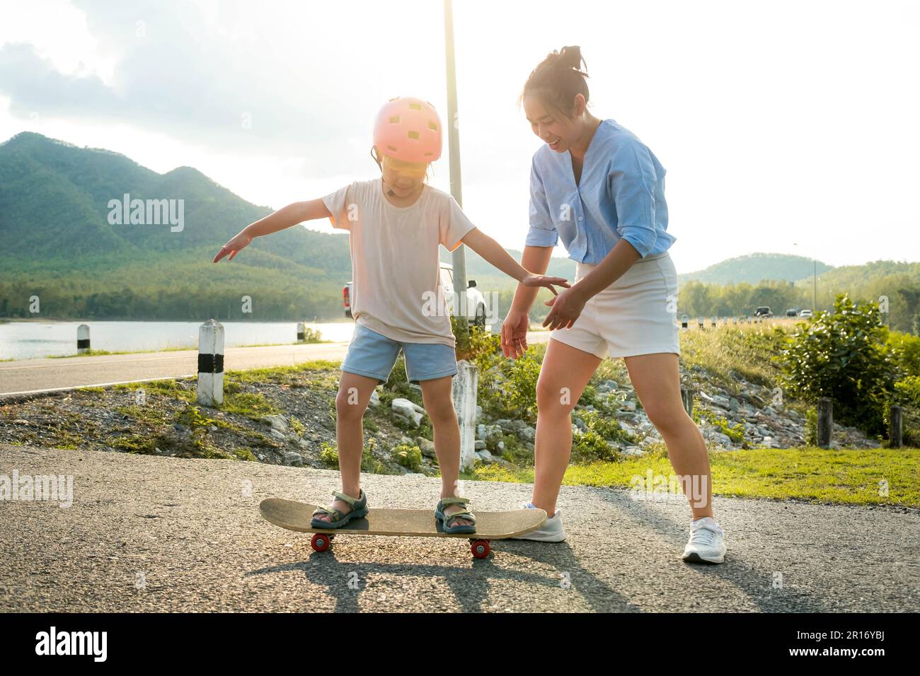 Mother teaching her daughter how to skateboard in the park. Child