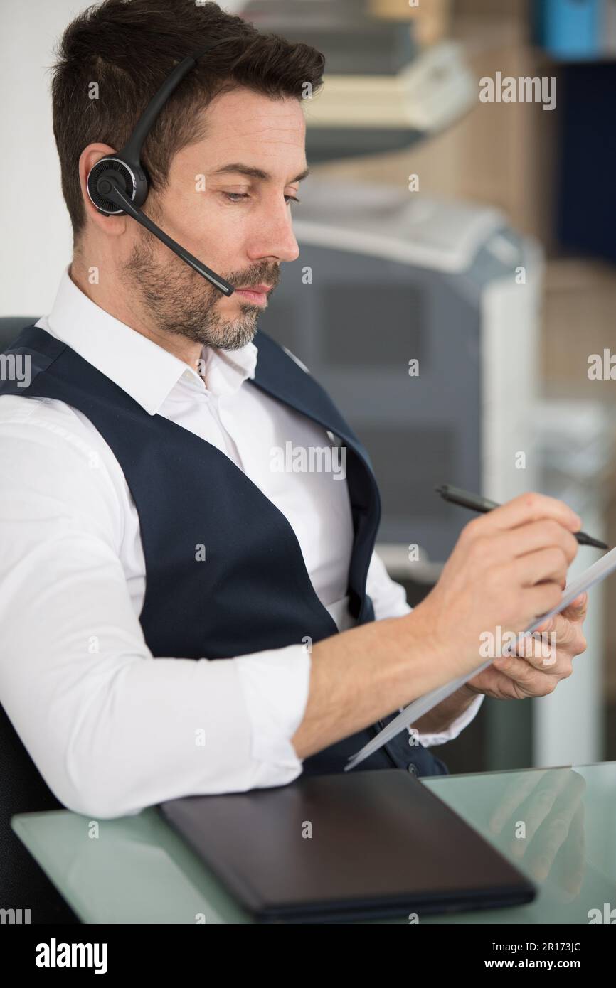 businessman wearing headset with microphone taking notes Stock Photo