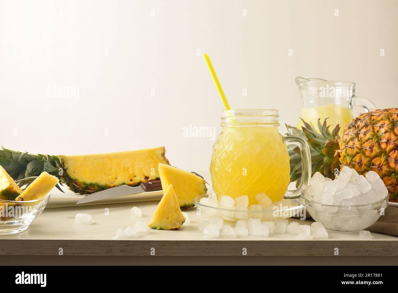 Full glass of pineapple drink with ice on table with crushed ice and fruit and isolated background. Front view. Horizontal composition. Stock Photo