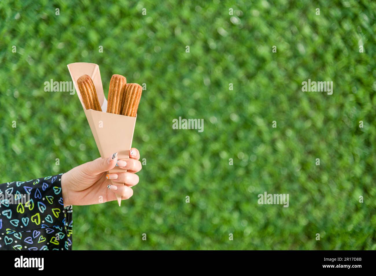 woman holding churros in cardboard box in front of green grass wall Stock Photo