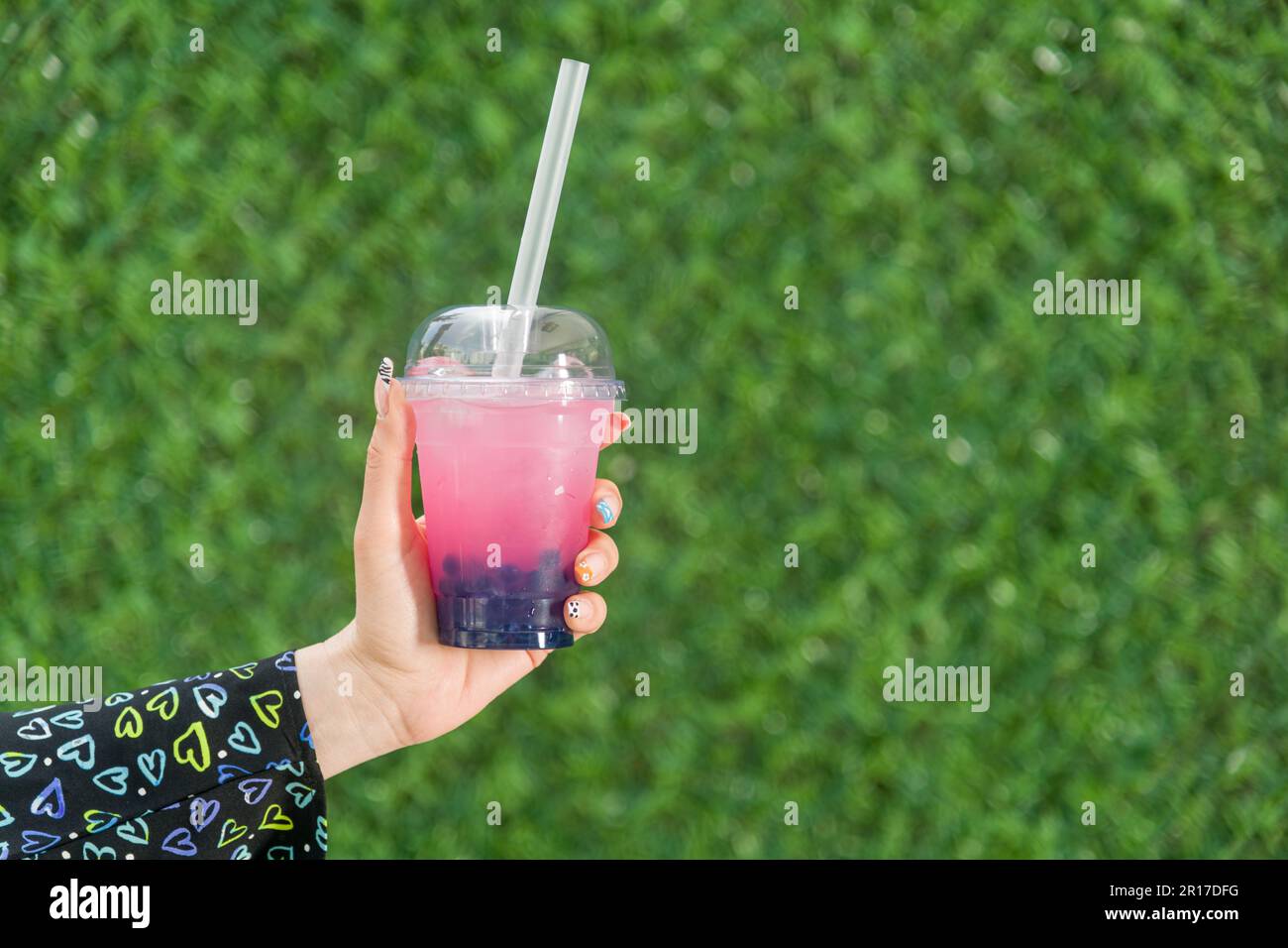 Woman holding bubble tea with lemonade in front of green grass wall Stock Photo