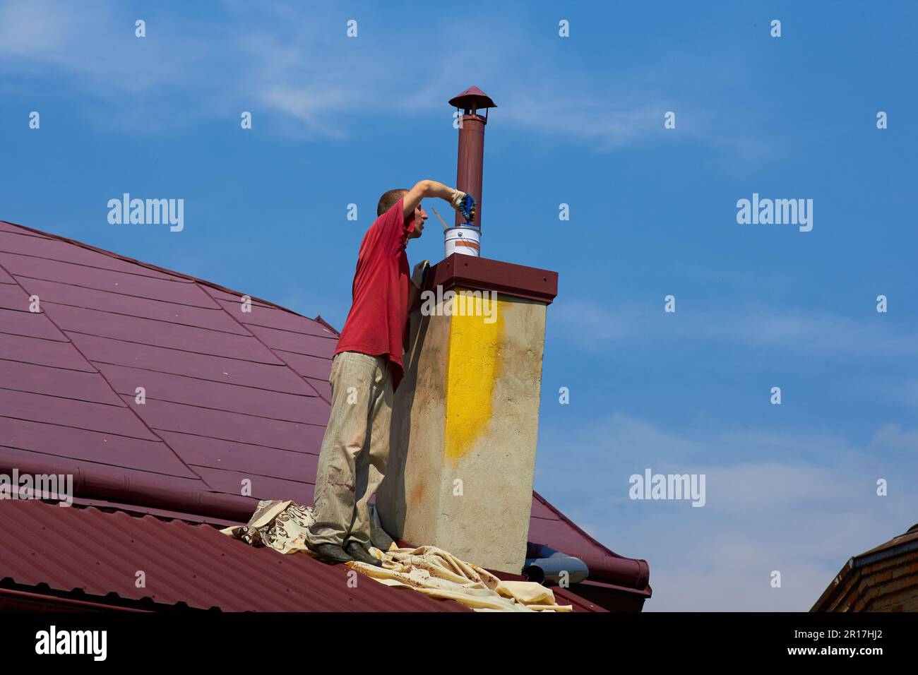 in dirty clothes a man paints a chimney on the roof Stock Photo