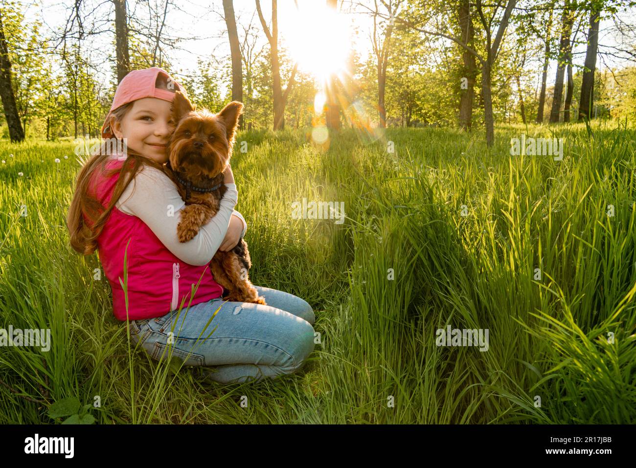 A cheerful girl sits in the thick green grass with her dog against the ...