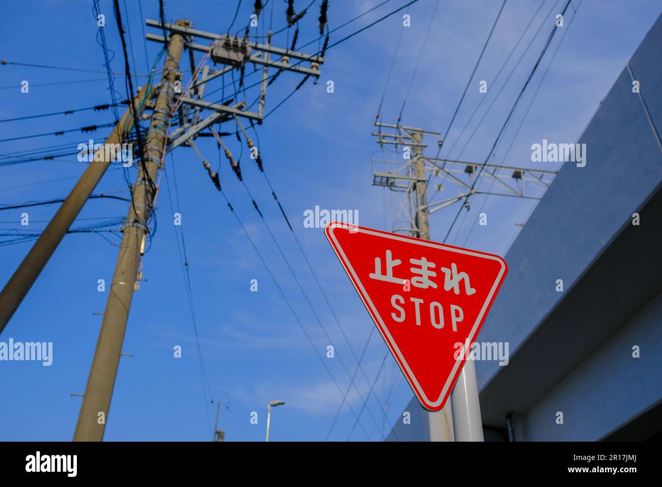 Traffic Stop Sign in both English and Japanese against a blue sky, with electricity poles in the background. Stock Photo