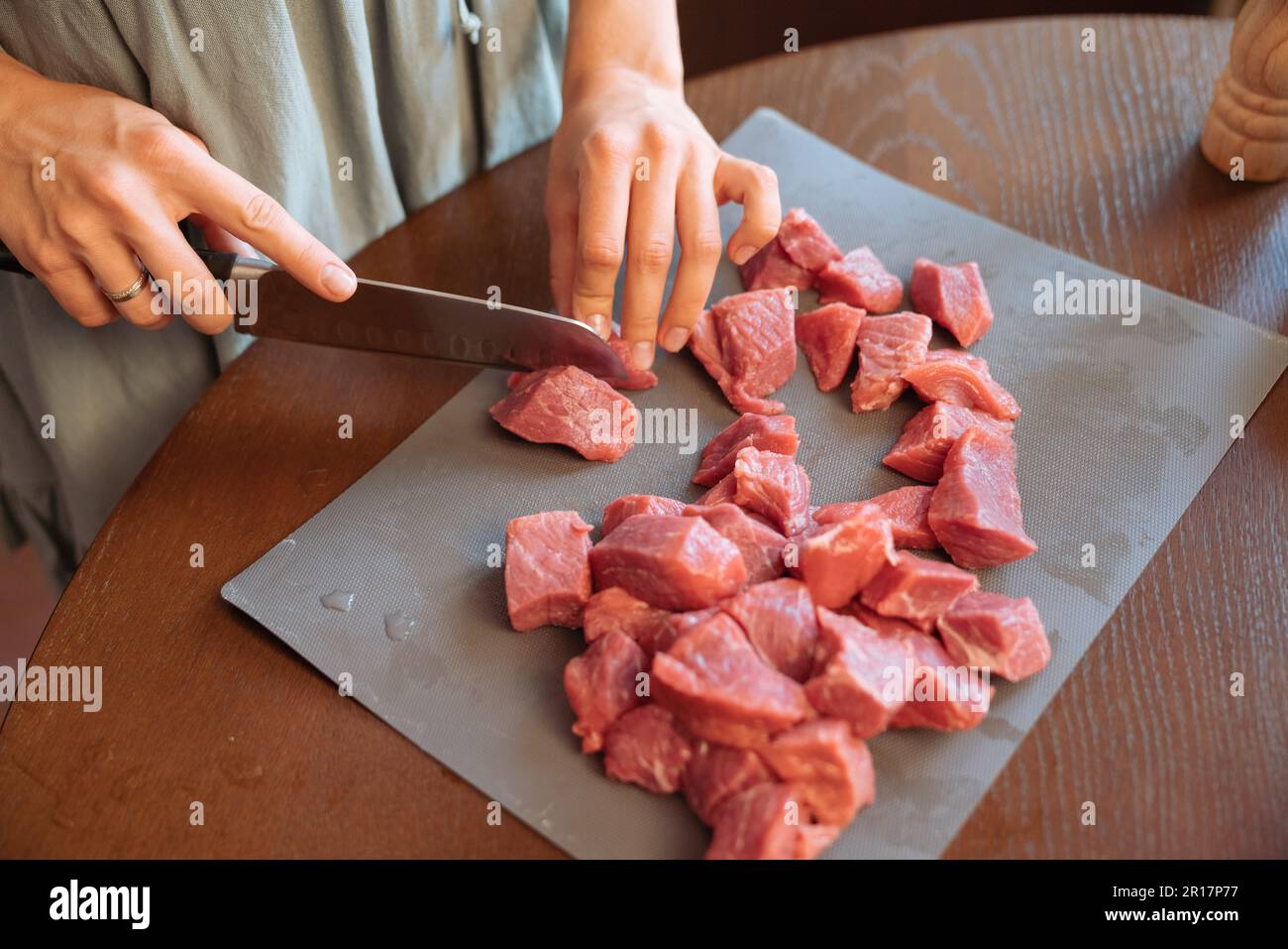 Woman's hands cutting beef pieces on a wooden table Stock Photo