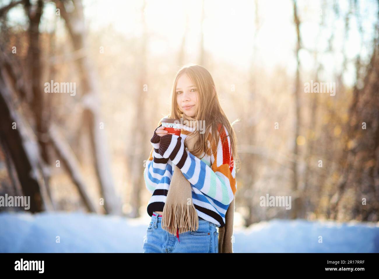 Beautiful tween girl holding coffee cup outdoors on sunny winter day. Stock Photo