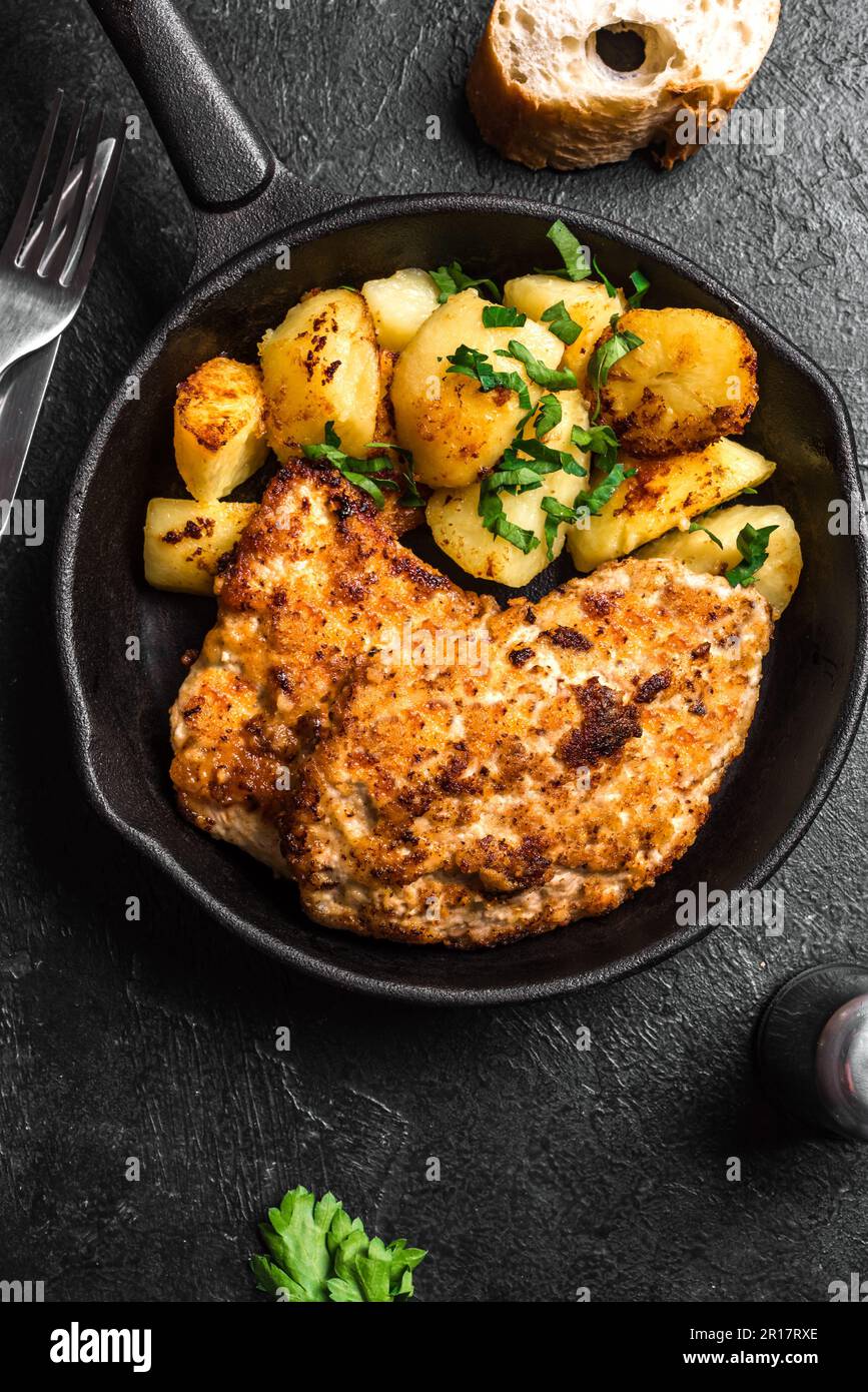 German schnitzel with roasted potatoes on rustic black cast iron pan