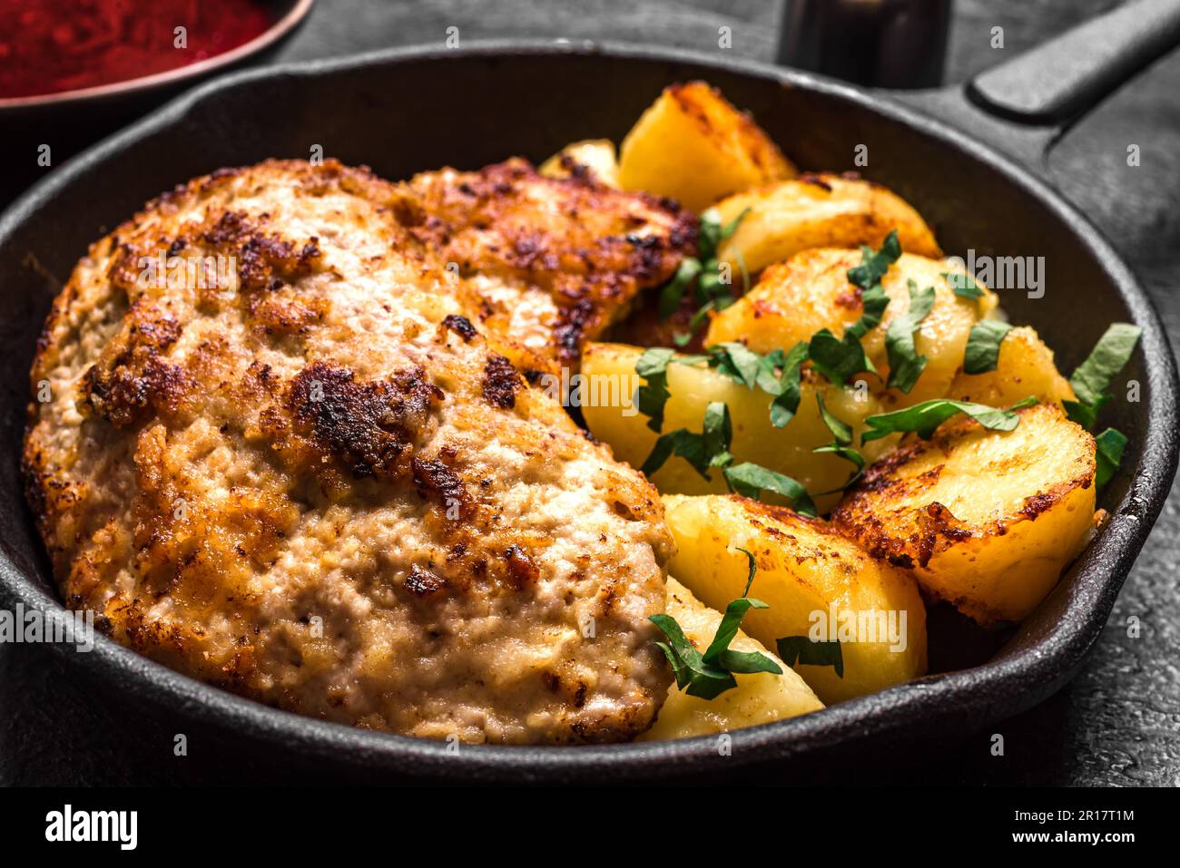 German schnitzel with roasted potatoes on black cast iron pan. Homemade