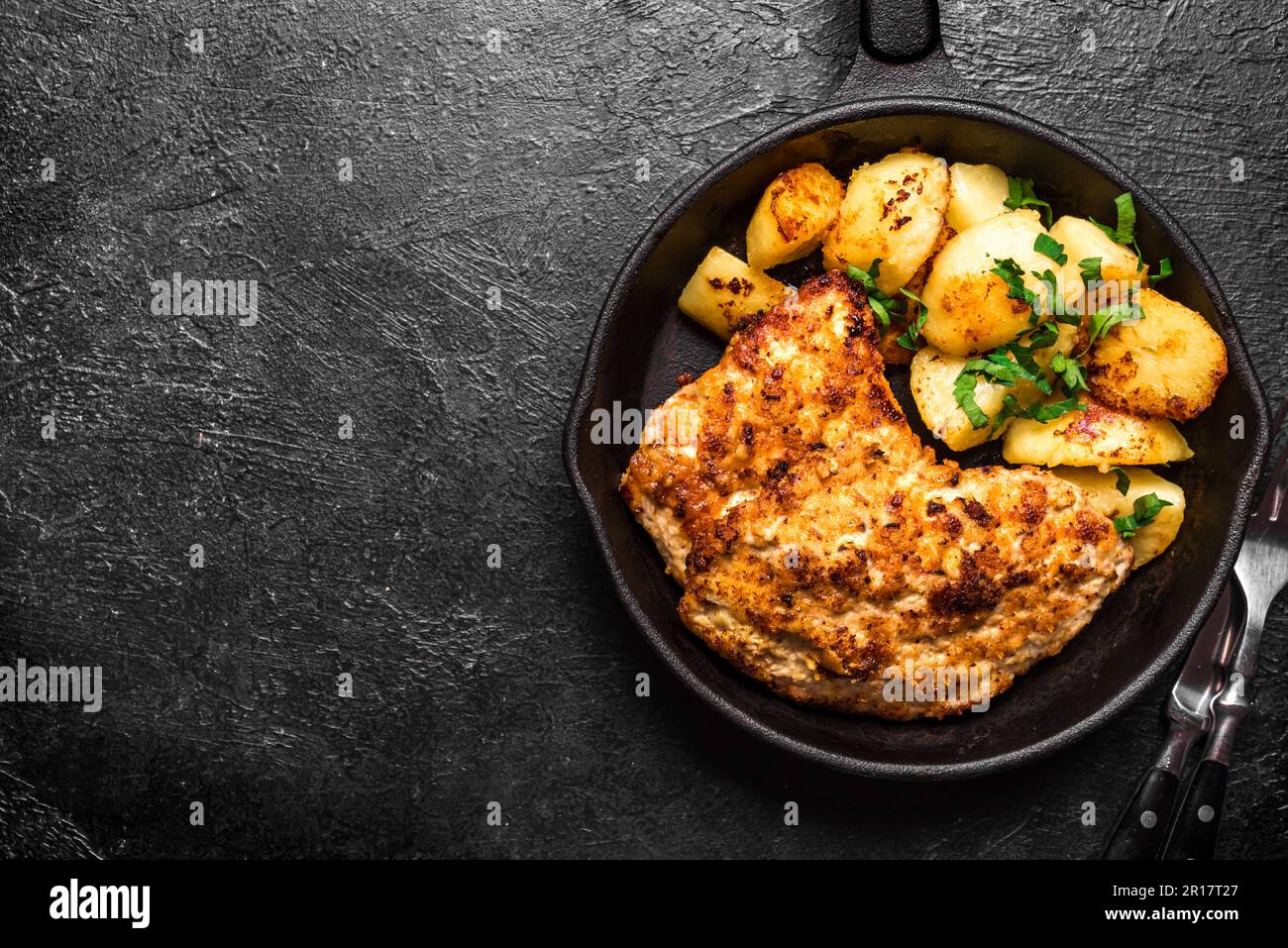 German schnitzel with roasted potatoes on black cast iron pan, copy