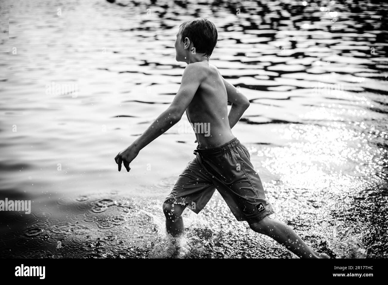 Boy splashing through lake during summer evening Stock Photo