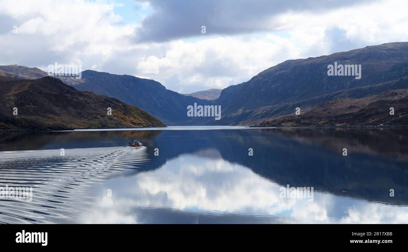 A small motor boat cuts across the glassy water of Loch Glann Dubh, Kylesku in the Scottish Highlands. Stock Photo