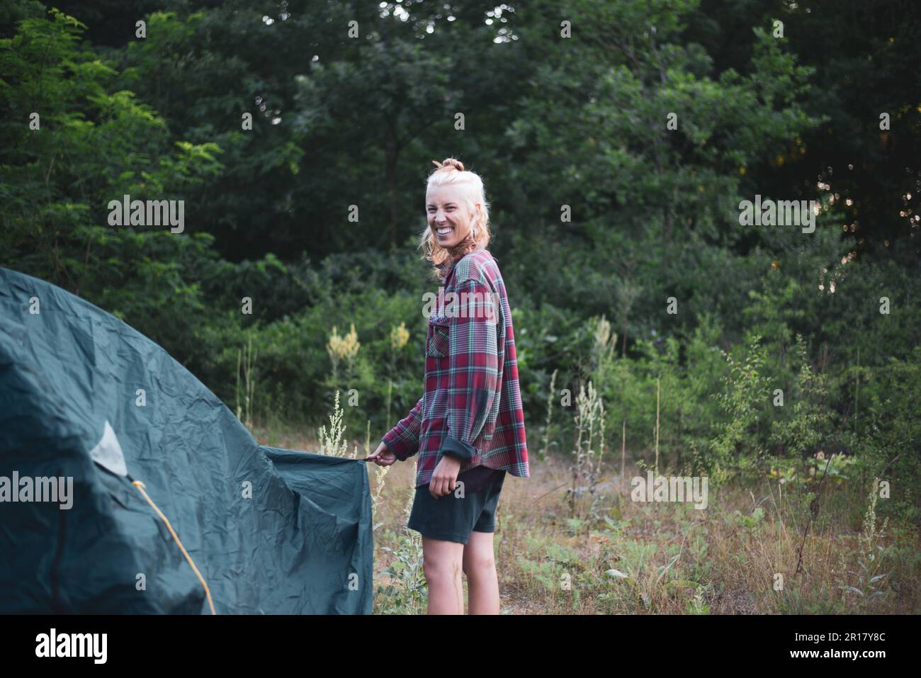 blonde european woman smiles cheekily setting up camp tent Stock Photo