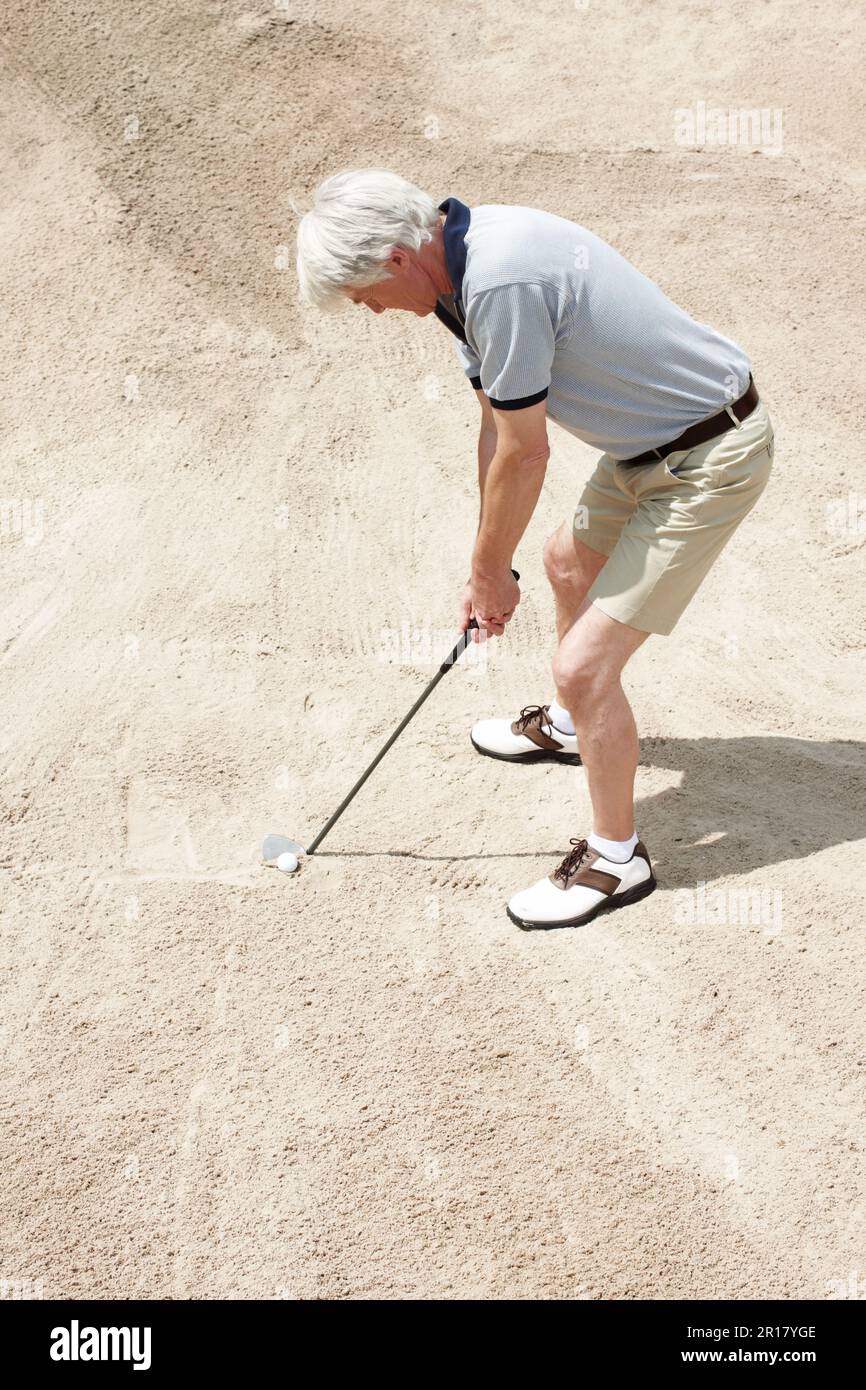 Stuck in the sand trap. Senior man trying to hit his ball out of the
