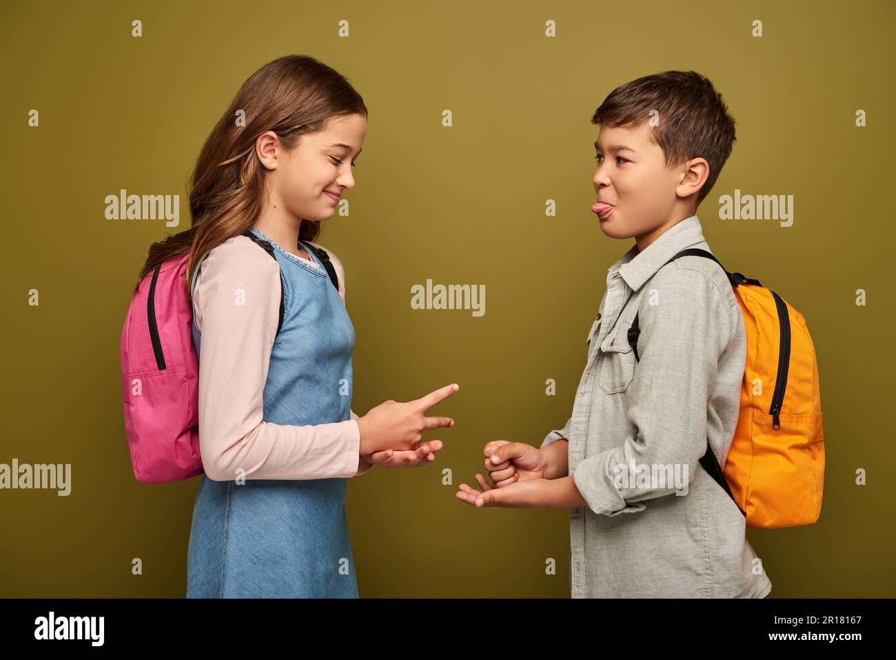 funny multiethnic kids with backpacks smiling and playing rock paper