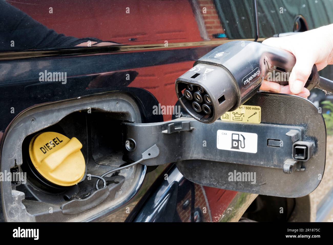 Connector for an electric vehicle charger next to the diesel tank filler cap of a car using fossil fuel. Stock Photo