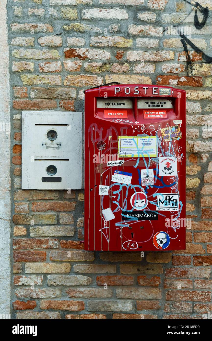 Sticker covered red mailbox next to an old intercom on a brick wall, Venice, Veneto, Italy Stock Photo