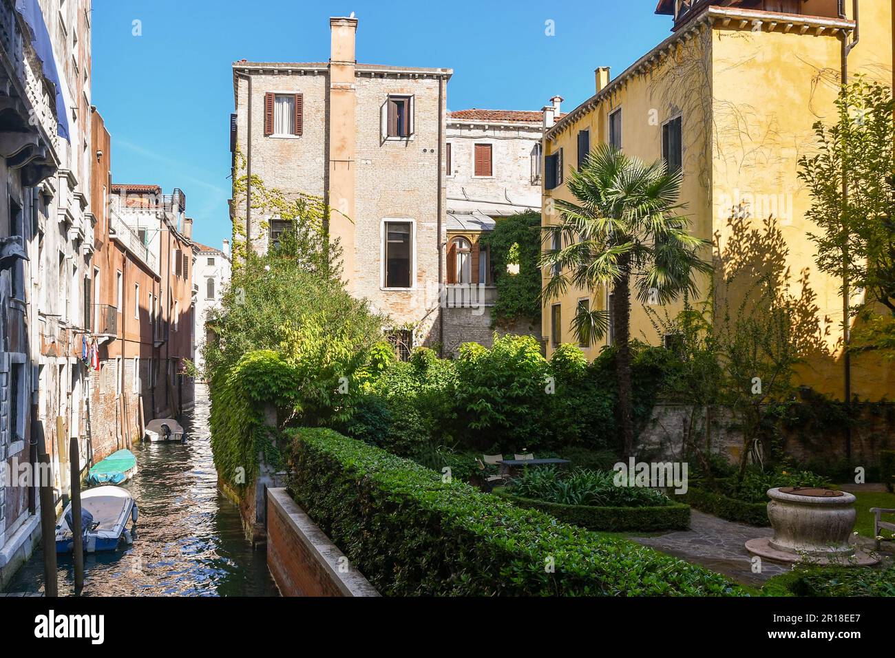 Beautiful garden with an old well and a palm tree overlooking the Rio de Cà Michiel in the sestiere of San Marco in summer, Venice, Veneto, Italy Stock Photo