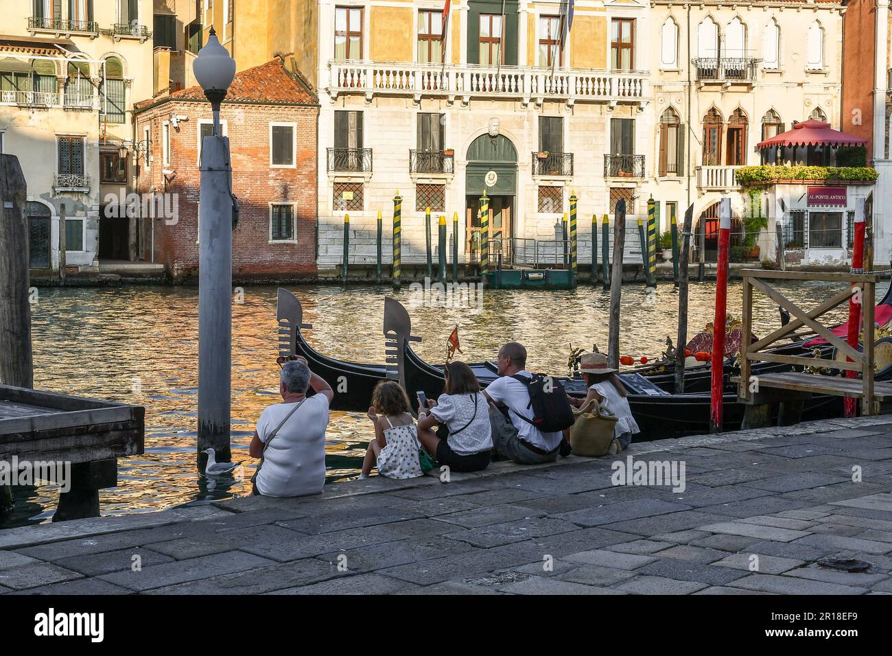 A family of tourists resting on the shore of the Grand Canal in summer, the main waterway of Venice, Veneto, Italy Stock Photo