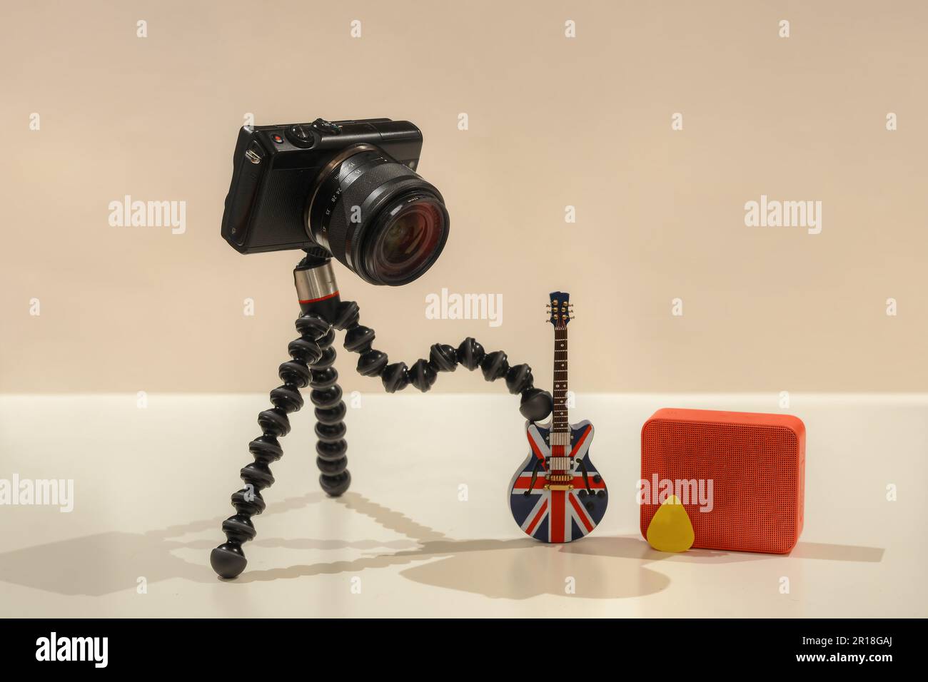 A photo of a camera playing electric guitar with a orange amplifier on the background with white background texture and a yellow pick Stock Photo