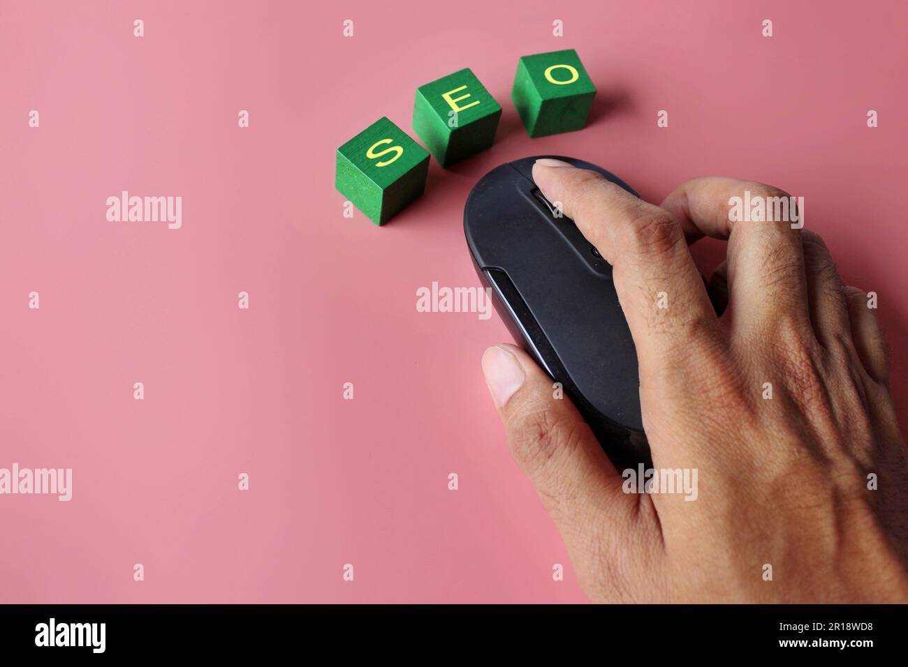 Hand click computer mouse with text SEO on pink background. Search engine optimization concept. Stock Photo