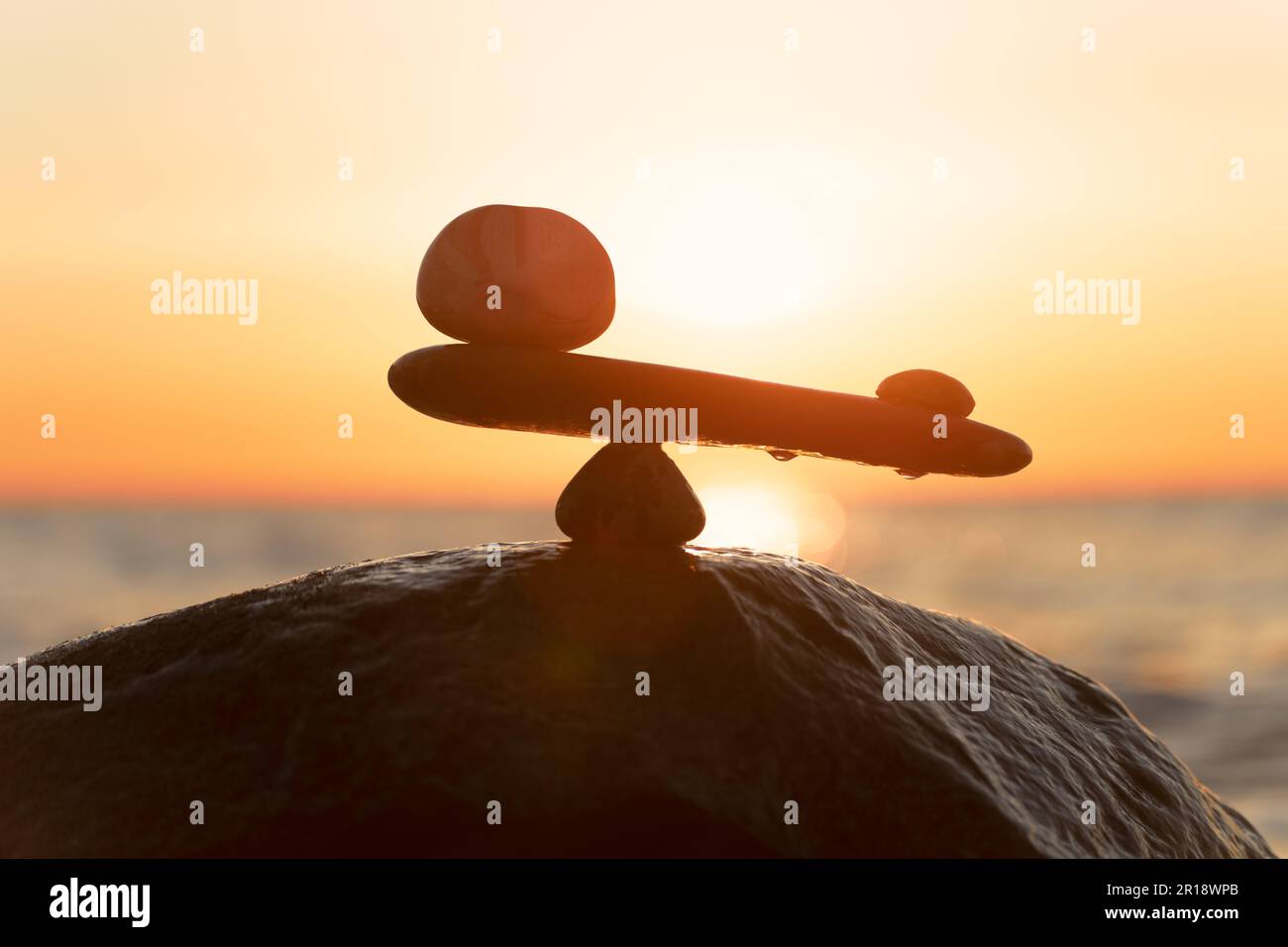 Imbalance of forces - natural scales of stones ( in imbalance) at the sea to the orange sunset - symbol photo Stock Photo