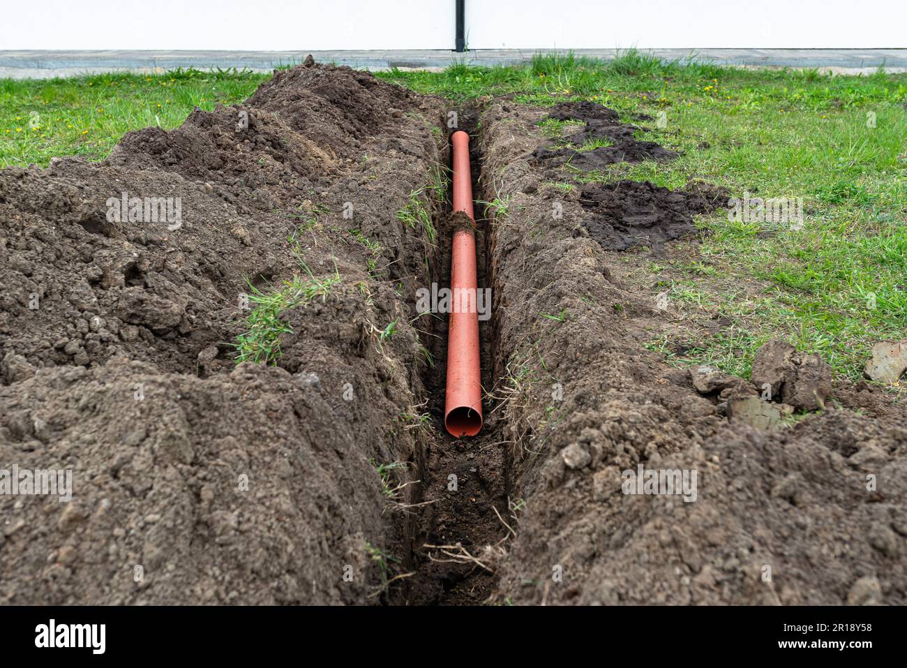 Orange PVC pipe buried in the ground connected to the gutter, used to connect to the drainage pipe. Stock Photo