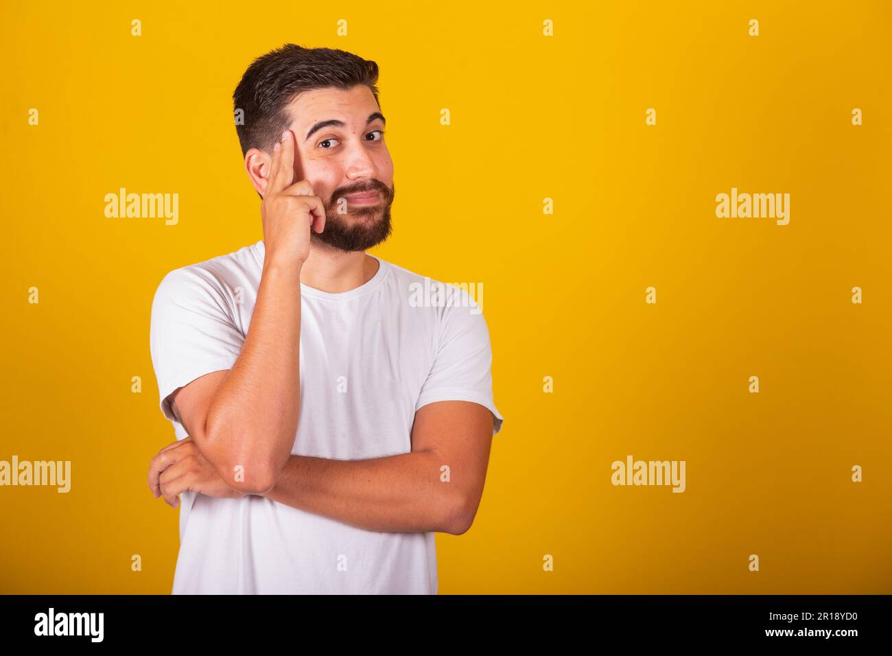 Brazilian Latin American man with hands on forehead and chin representing thought, pensive, doubt, questioning, decision, uncertainty, yellow backgrou Stock Photo
