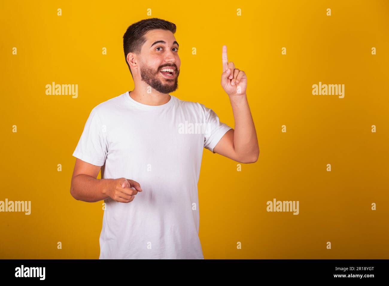 Brazilian Latin American man, with raised finger representing idea, answer, discovered, knew, solved. Concept of idea, creation. Yellow background Stock Photo