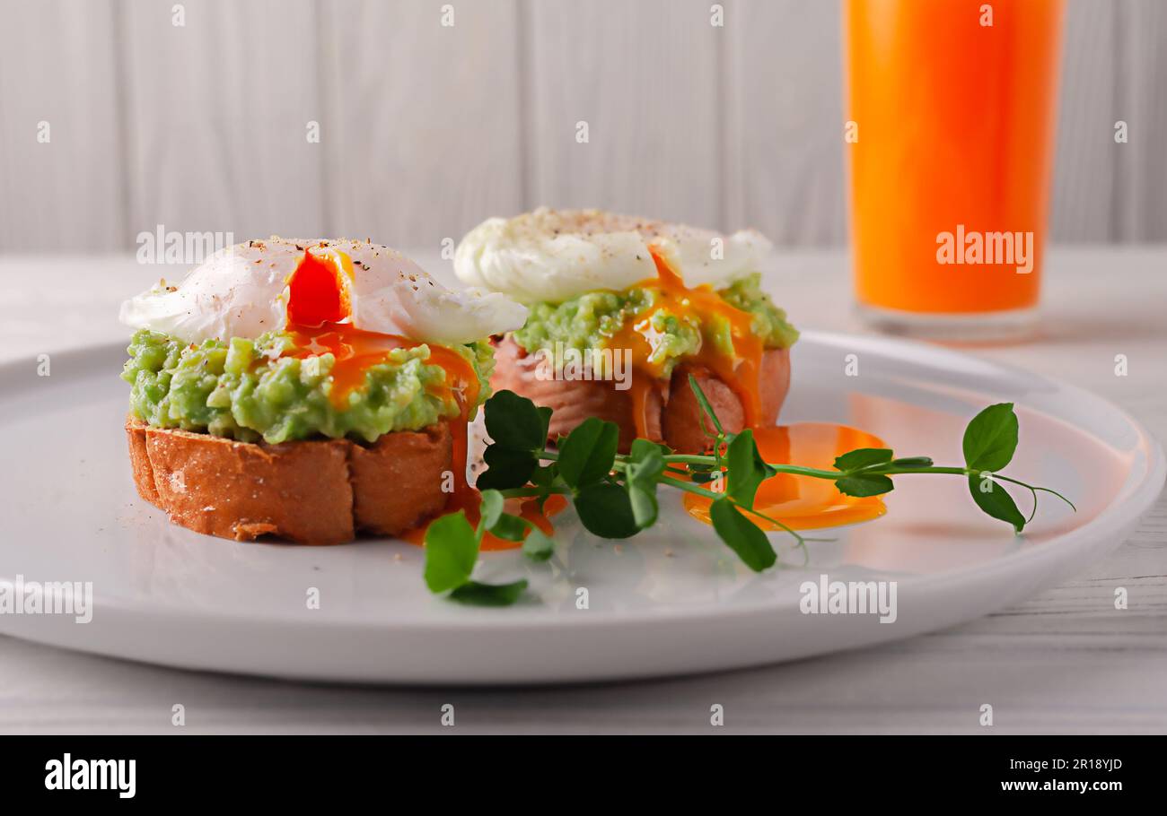 Toasted bread with avocado, poached egg and fruit juice on a white wooden table. healthy diet food. European breakfast. Stock Photo