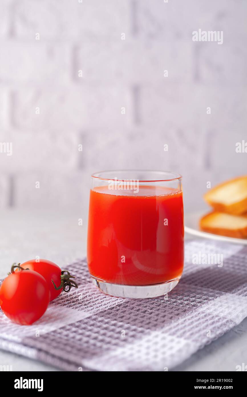 Against the background of a white brick wall, a glass of tomato juice with vegetables Stock Photo