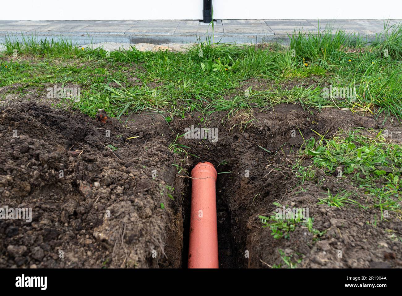 Orange PVC pipe buried in the ground connected to the gutter, used to connect to the drainage pipe. Stock Photo