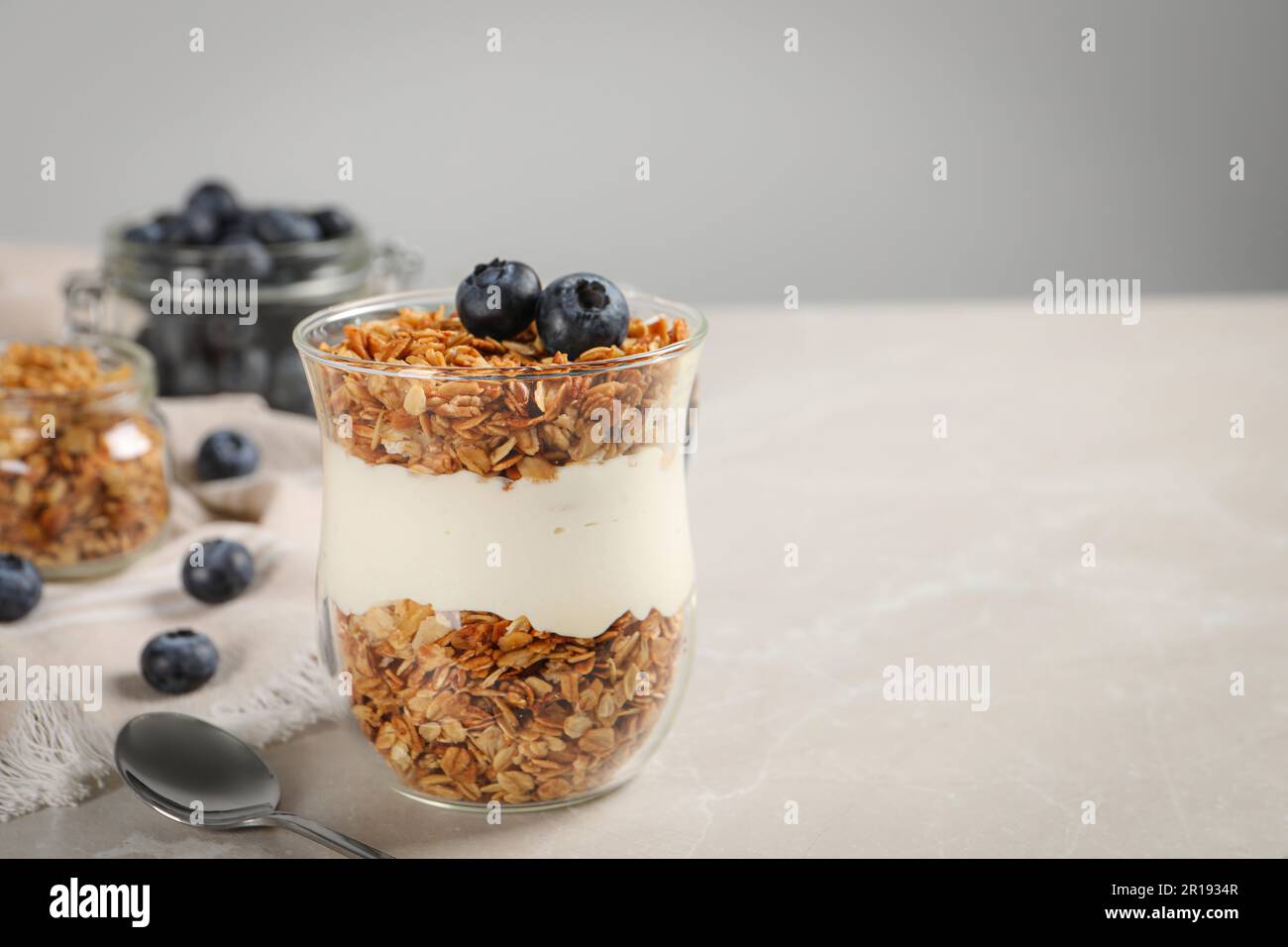 Glass of yogurt with granola and blueberries on grey marble table, closeup. Space for text Stock Photo