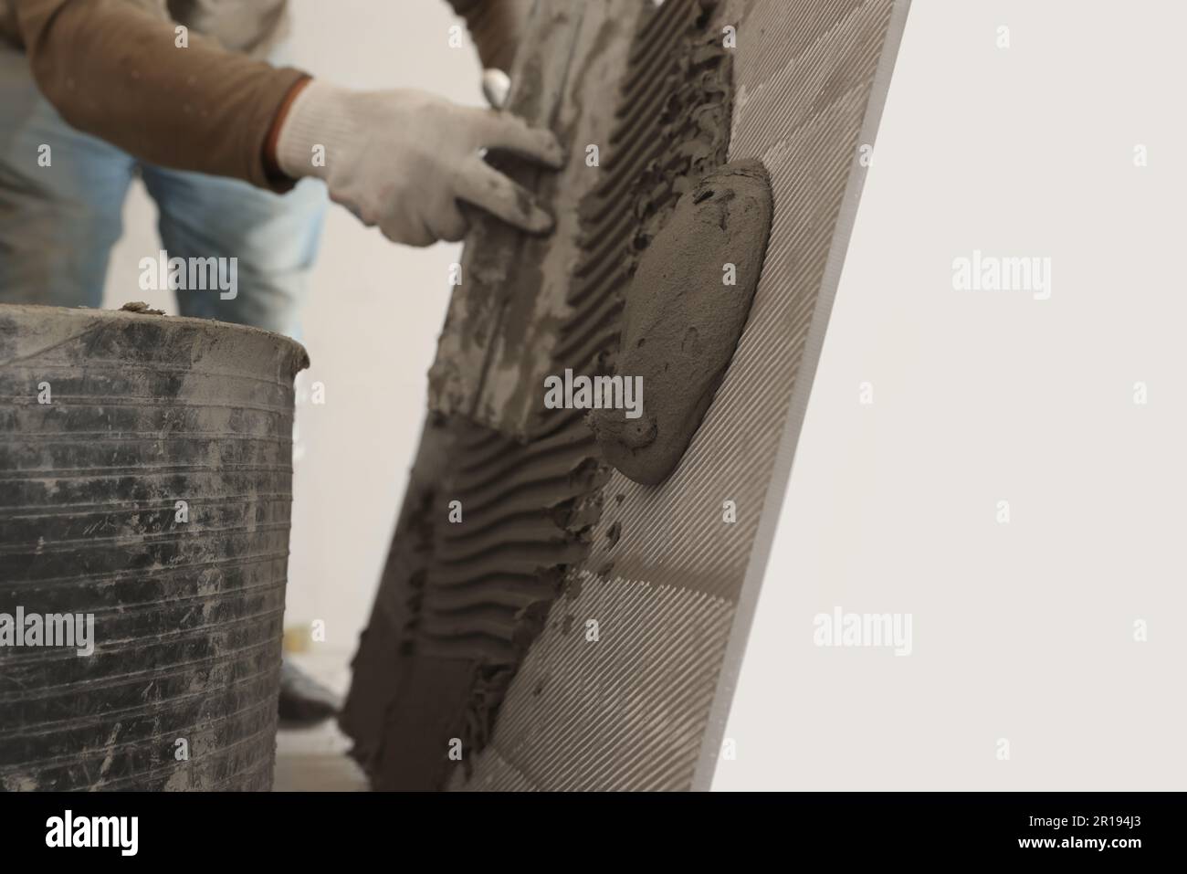 Worker applying cement on wall tile for installation indoors, closeup