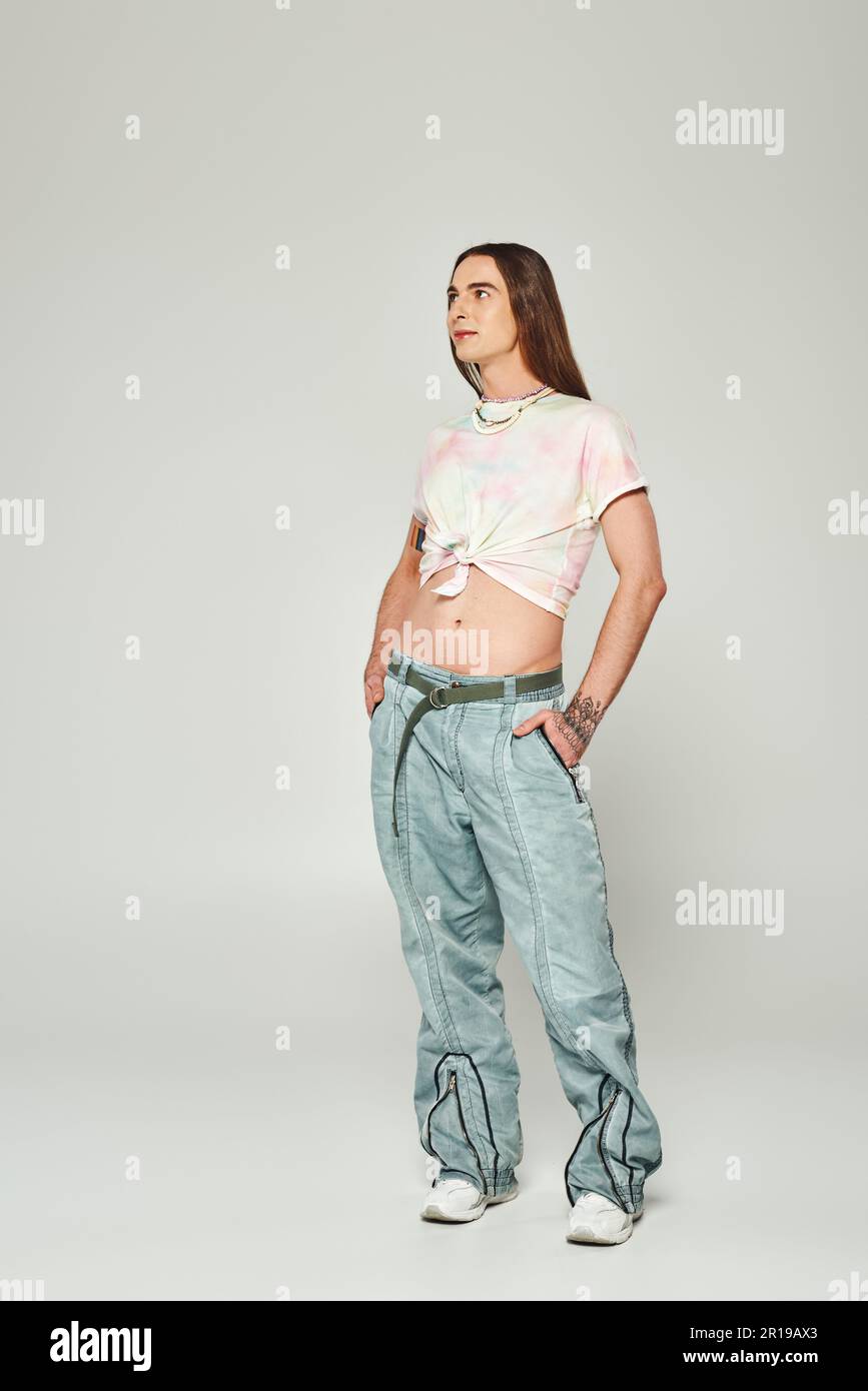 Full length of tattooed and long haired homosexual man holding hands in pockets of denim jeans and looking away during lgbt community pride celebratio Stock Photo