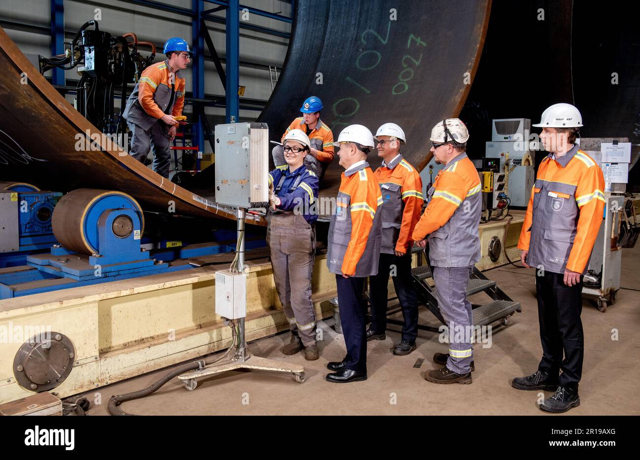 12 May 2023, Lower Saxony, Nordenham: Janina Patricia Schweitzer (l-r), a production employee at Steelwind Nordenham GmbH, shows German Chancellor Olaf Scholz (SPD), Andreas Liessem, Managing Director of Steelwind Nordenham GmbH, Jörg Redmer, a production employee, and Jonathan Weber, a member of the Board of Management of Dillinger Hüttenwerke AG, the function of the longitudinal seam welding machine used to manufacture steel foundations for wind turbines. Scholz visited the production of steel foundations, so-called monopiles, for wind turbines in offshore wind farms at Steelwind Nordenham G Stock Photo