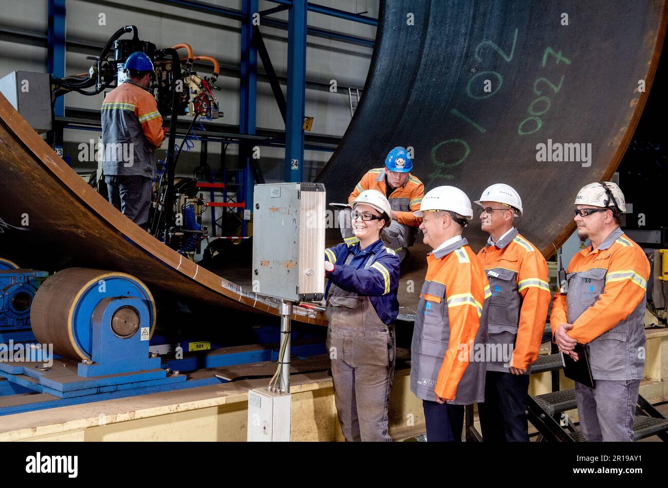 Nordenham, Germany. 12th May, 2023. Janina Patricia Schweitzer (l-r), a production employee at Steelwind Nordenham GmbH, shows German Chancellor Olaf Scholz (SPD), Andreas Liessem, managing director of Steelwind Nordenham GmbH, and Jörg Redmer, a production employee, the function of the longitudinal internal seam welding machine used to manufacture steel foundations for wind turbines. Scholz visited the production of steel foundations, so-called monopiles, for wind turbines in offshore wind farms at Steelwind Nordenham GmbH. Credit: Hauke-Christian Dittrich/dpa/Alamy Live News Stock Photo