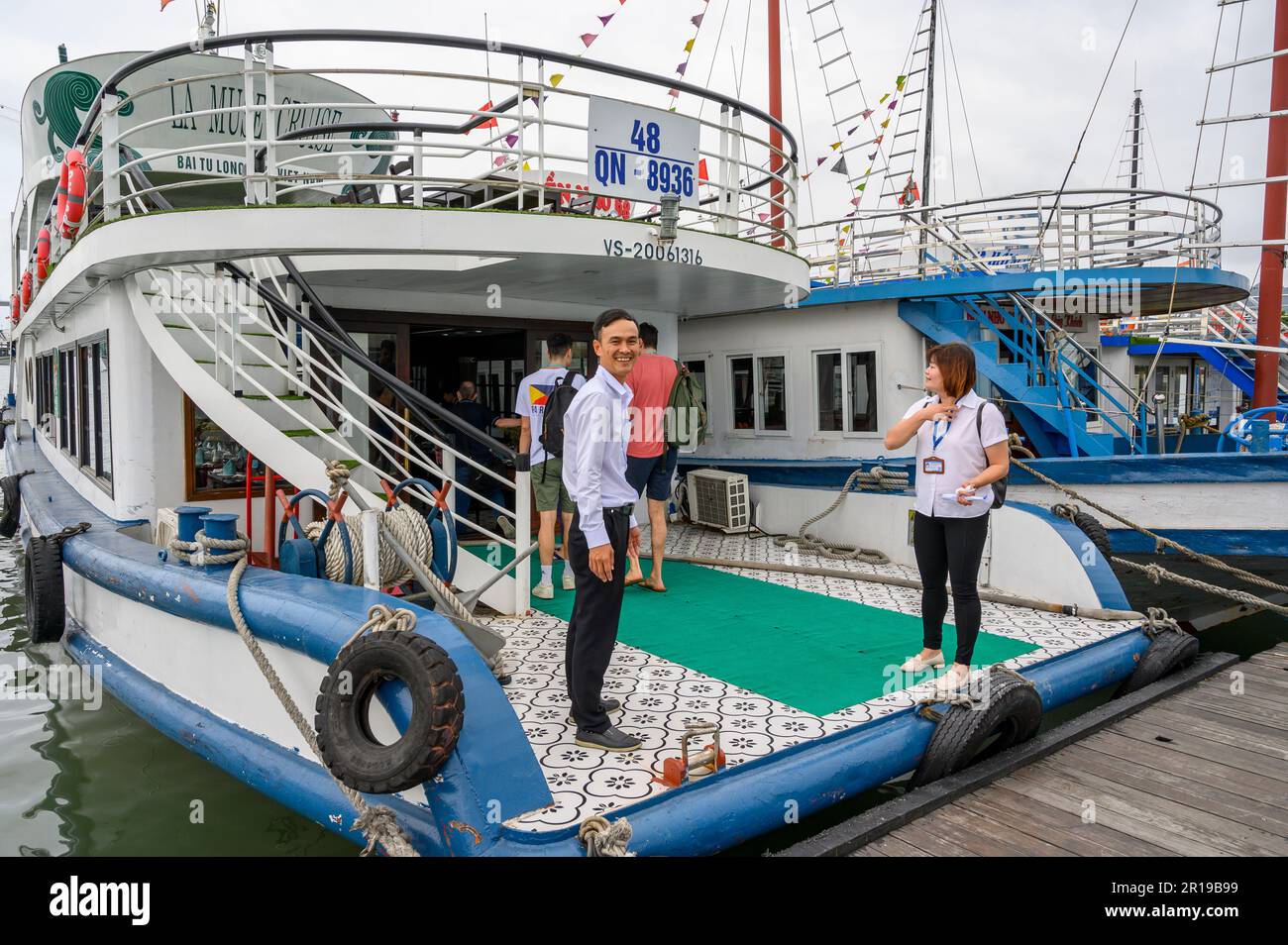 The captain and guide welcome passengers onto the La Muse Cruise boat ready to sail into the Bai Tu Long Bay in the Halong Bay archipelago, Vietnam. Stock Photo